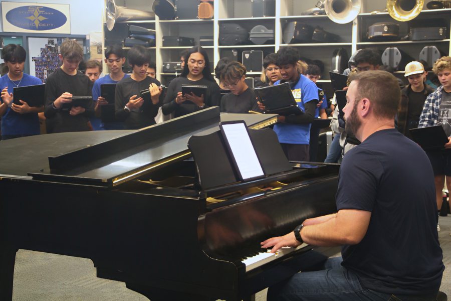 Music director Johnny Erdman plays the piano as his choir students sing along and harmonize.